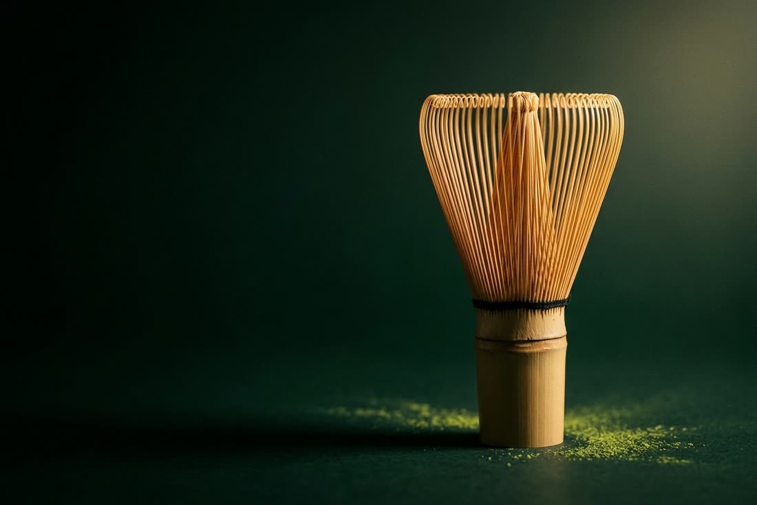 A handmade bamboo matcha whisk standing upright beside scattered matcha powder